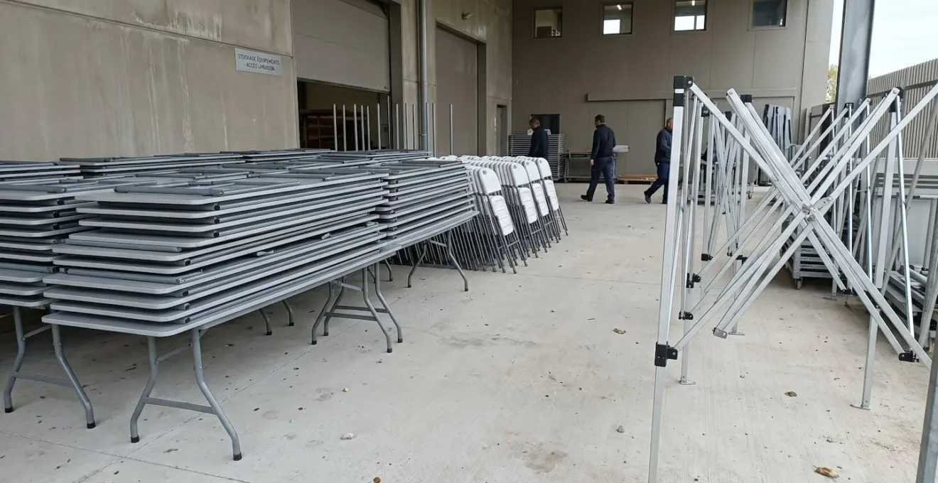 Point de retrait de matériel événementiel avec mobilier pliant et structure de barnum rangés en extérieur